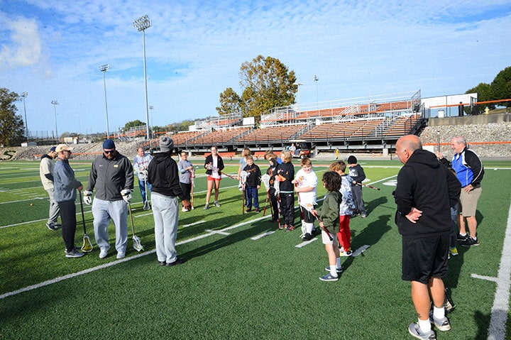 A group of lacrosse coaches teaching young students during a clinic.