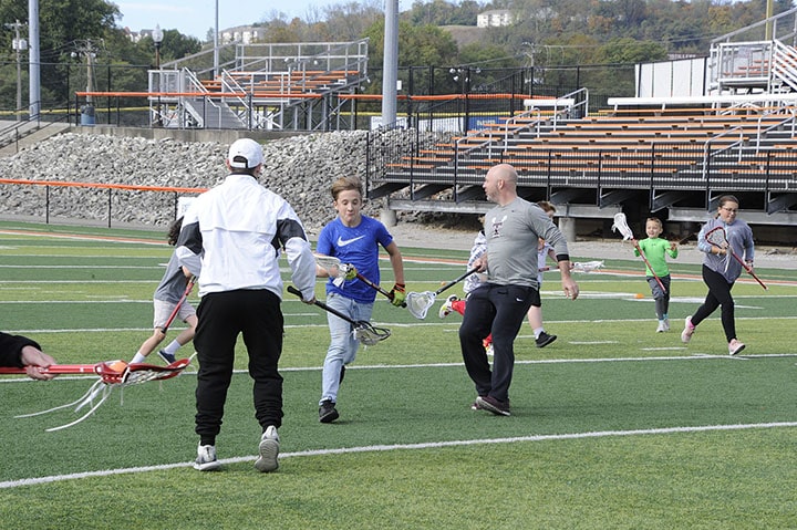 Two lacrosse coaches working
          with a young participant at a TryLax event at Lawrenceburg High School.