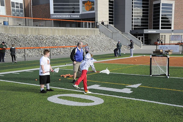 A lacrosse coach working with two young athletes who are learning to shoot a
          lacrosse ball into a net.