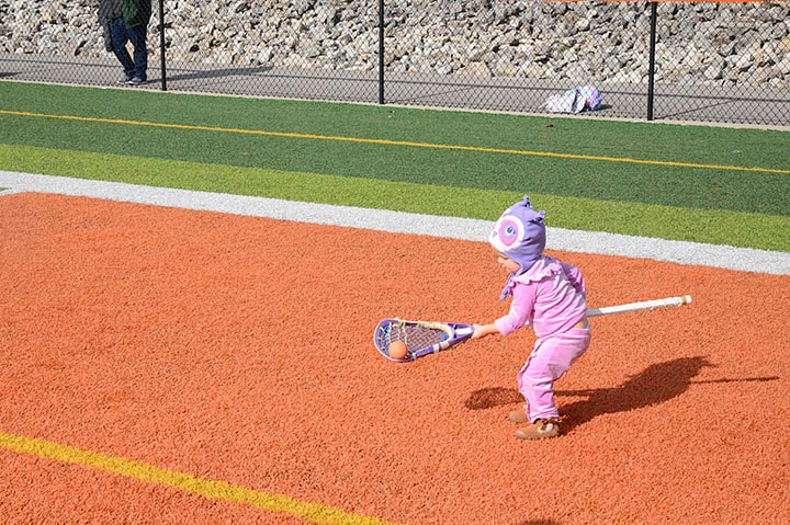 A toddler passing a ball with a full-sized lacrosse stick.